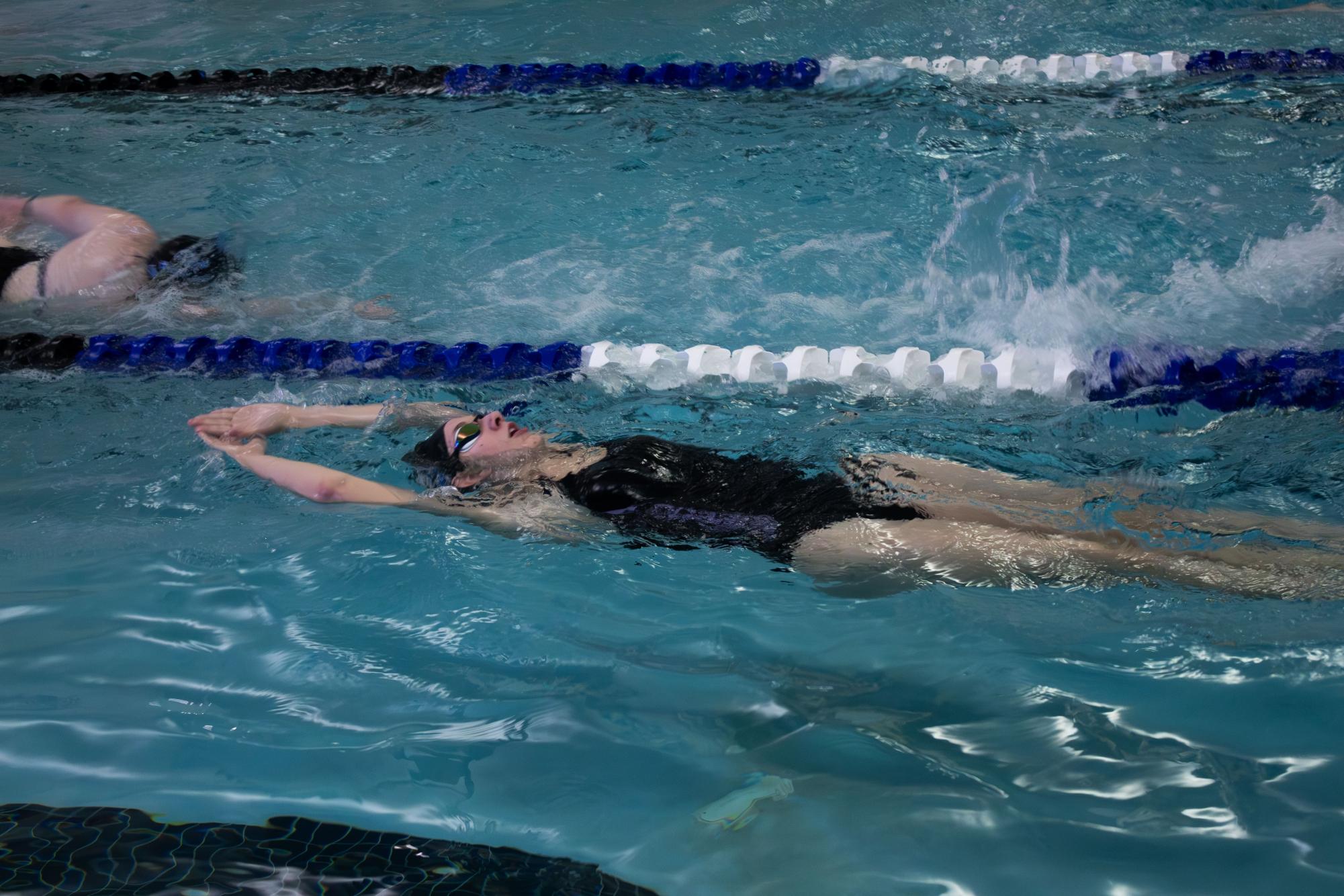 A swimmer glides through a backstroke drill, maintaining body alignment and tempo as coaches observe stroke fundamentals.
